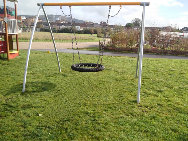On the playground, under the tire-shaped swing, there are grass protection mats through which the grass grows lushly.