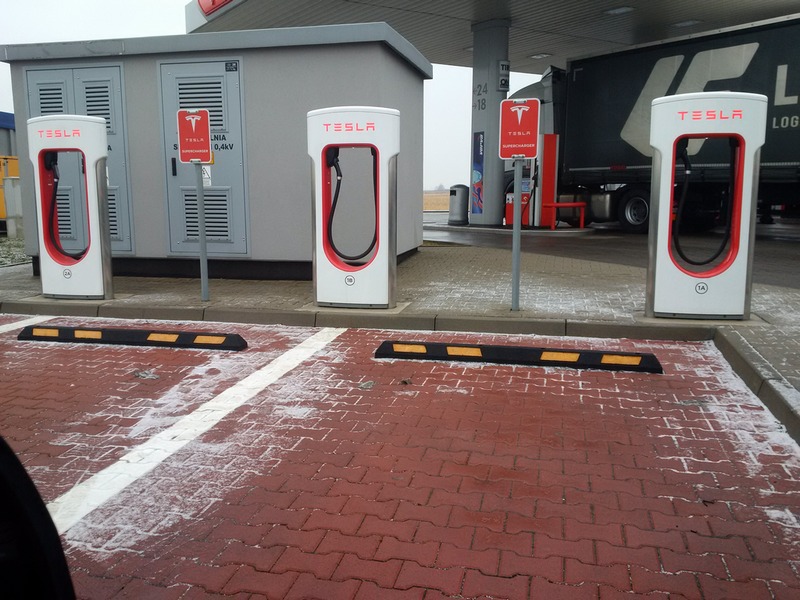 Parkplatz mit Tesla-Ladestationen. Auf Parkplätzen sind Parkschranken angebracht.