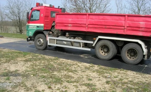 Červený sklápěč stojí na deskách WS MudGuard, které chrání zem